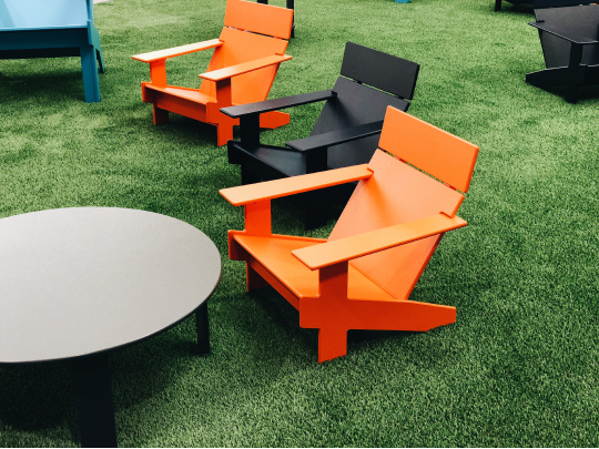 Outdoor seating area with modern orange and black chairs placed on artificial grass, along with a round table.